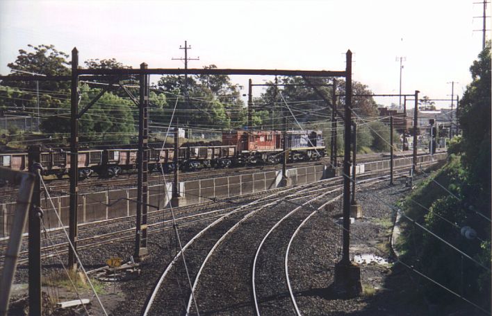 
A view showing Lidcombe Goods Junction.  Rookwood Cemetery is behind the
trees in the background, and Lidcombe station is in the right distance.
On the main suburban lines is a ballast train worked by a pair of 48s
