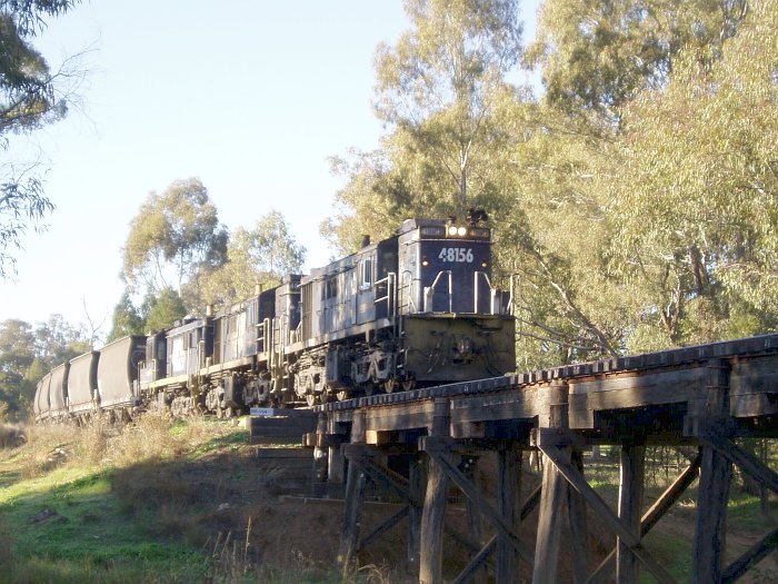 A wheat train headed by 3 48-class locos is about to cross a wooden trestle bridge.