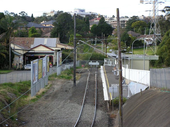 Close-up from the Cumberland Hwy (Pennant Hills Rd) overpass, showing that the produce siding and former double track mainline are barely recognisable inside the current perway area. You can see the catenary continuing beyond the station, and the awning for the old produce siding.
