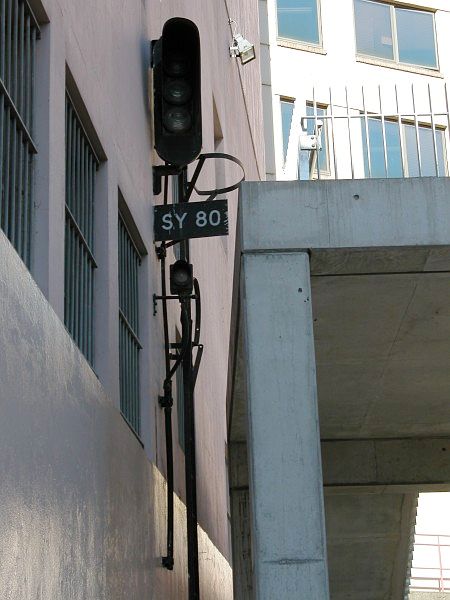 
A relic of busier days. An isolated signal now disconnected is still
in its original position attached to a building near the entrance to
the Broadway tunnel on the former Darling Harbour line. The signal is
now tightly sandwiched between the wall and a new pedestrian
overpass.
