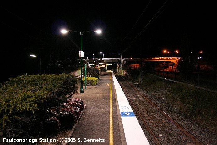 A night-time photo taken from the Sydney end of Faulconbridge platform 1 facing in a southerly direction looking along the Up main. The footbridge over the highway is visible in right of photo.