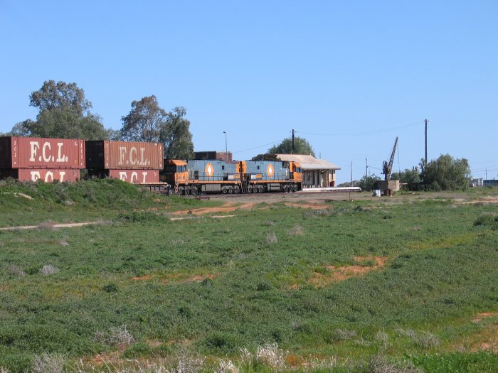 A westbound freighter with double-stacked containers passes through the station.