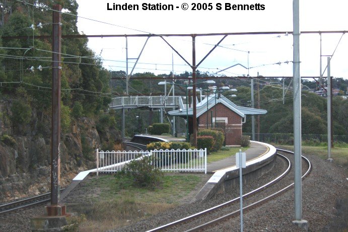 A photo taken looking in a westerly direction showing the Sydney end of platform and buildings at Linden and the tight radius of the curve it is built on. To the right and centre rear of the photo, the homes of residents of Linden can be seen through the maze of overhead wires and staunchions.
