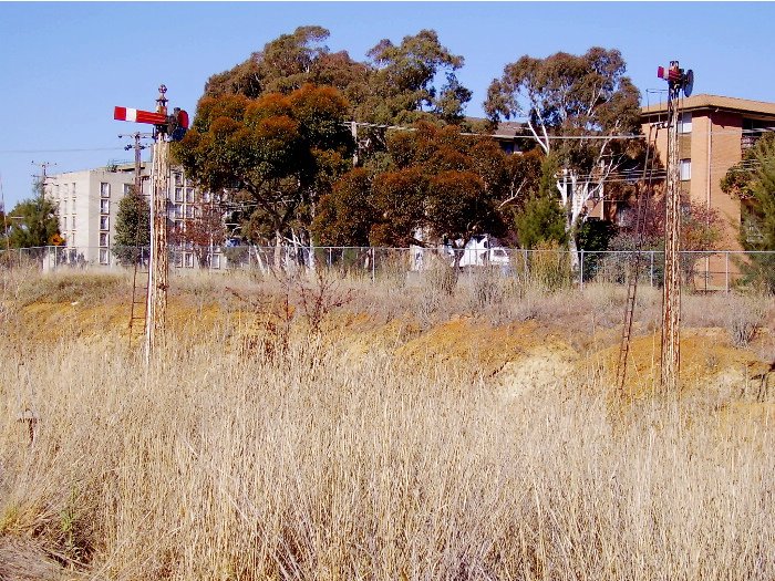A close-up of the signals at the junction of the Canberra and Bombala branch lines just before these enter Queanbeyan station.  Both lines pass through cutting as they approach the station necessitating tall masts; the Canberra line being the left signal and the Bombala one the right.