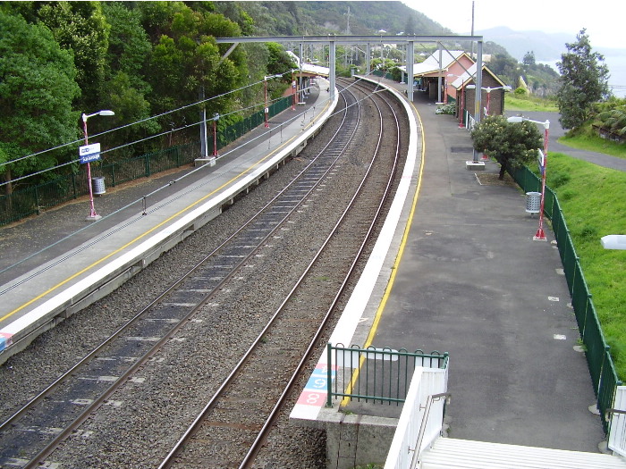 The view from the footbridge at the down end of Scarborough station showing the general layout of platforms and buildings.  The curved platforms is necessitated by the line weaving its way along the side of the Illawarra escarpment with steep cliffs on either side.
