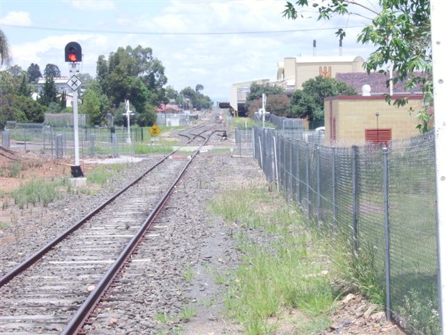 Looking in the Down direction from the end of the platform. The rationalised yard sees a single track (formerly the Platform Road) at the station . Beyond the Brisbane Street level crossing is the main line on the left. The track (and on the same alignment as the Platform Road) on the right was formerly used for freight at the factory's loading dock.
