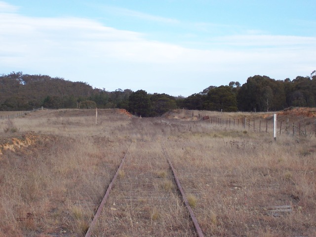 The view  looking towards Goulburn. The Station and platform are marked with the faded white post on the left and the 242km peg on the right with its number plate removed. Sleepers of the passing loop can been seen at the bottom right.