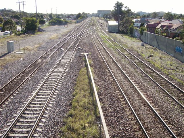 The view looking west of the Down and Up Main lies and the Down and Up Coal lines.        In the distance to the right of the Up Coal line is the points leading to the siding to the industrial building formerly known as Commonwealth Steel. CommSteel was a large supplier of railway wheels and axles in the past and owned its own shunting loco. This siding has since been disconnected . A goods yards with platform and usual structures formerly occupied the area to the left of the photo.