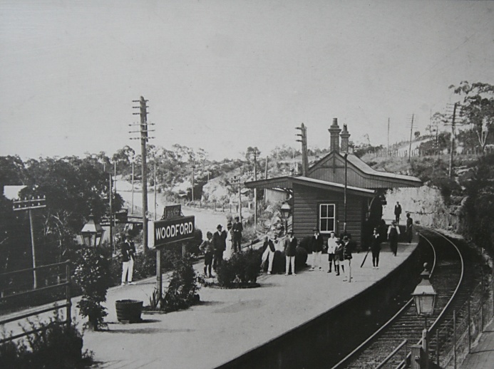 A photo of a photo held at National Trust's (NSW) Woodford Academy. It shows Woodford Station and the signal box which was removed in the late 1950's. The photo has been estimated to have been taken circa 1919, dated from the people and the items in the photo.  The original single line cutting dating back to 1867 and by passed by 1896 can be seen slightly above and to the right of the D on the Woodford sign on the platform. The original highway can also be seen behind this sign which now forms the lower carpark at Woodford Station. At least 2 station staff can also be seen in this photo.
